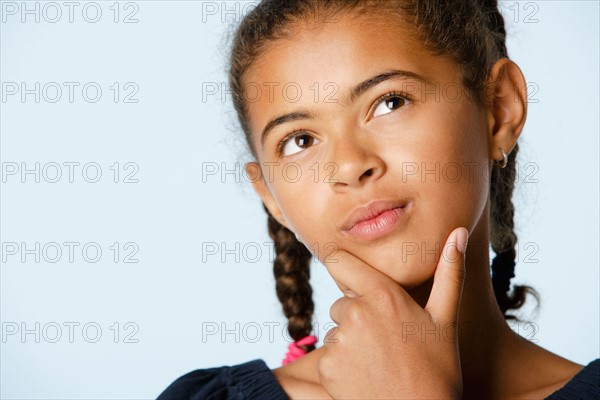 Studio portrait of girl (10-11) with hand on chin, looking up. Photo : Rob Lewine