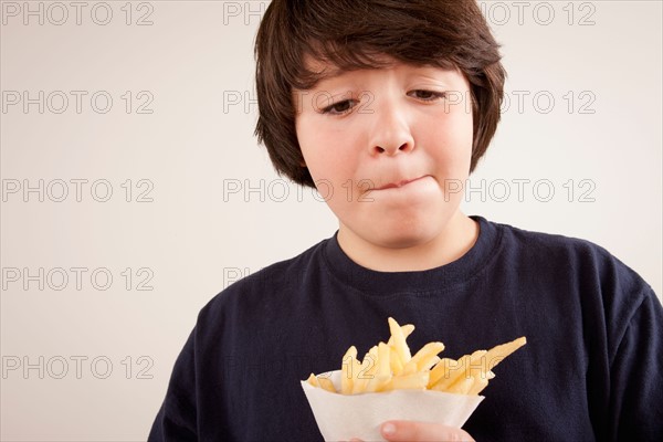 Studio portrait of boy (10-11) holding french fries. Photo : Rob Lewine