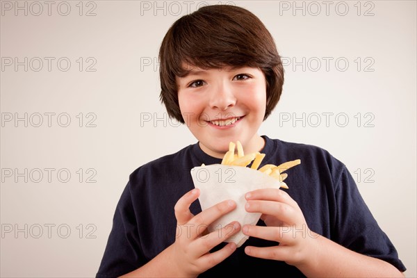 Studio portrait of boy (10-11) holding french fries. Photo : Rob Lewine