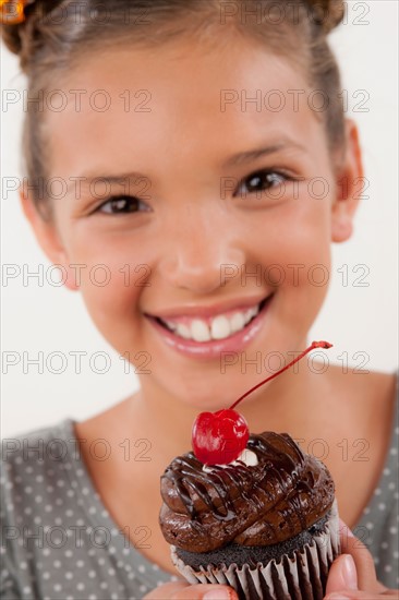 Studio portrait of girl (8-9) holding cake. Photo : Rob Lewine