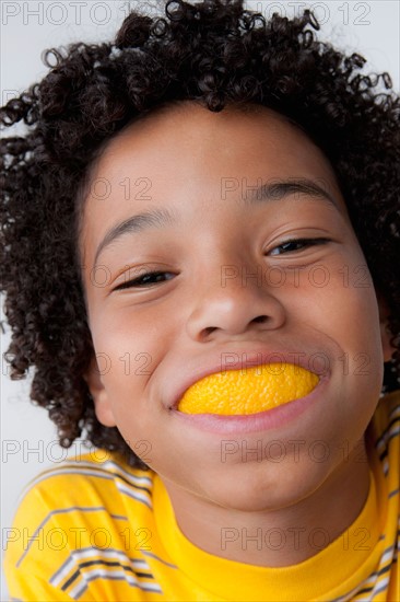 Studio portrait of boy (8-9) with slice of lemon in mouth. Photo: Rob Lewine