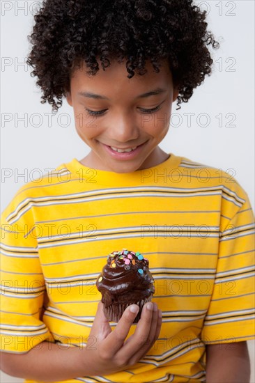 Studio portrait of boy (8-9) holding muffin. Photo : Rob Lewine