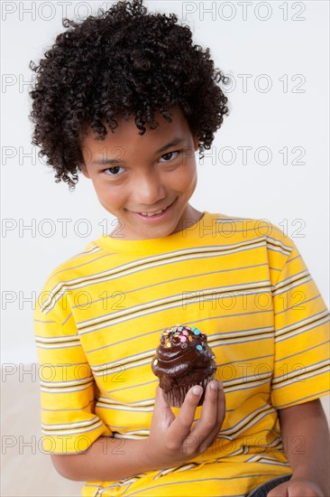 Studio portrait of boy (8-9) holding muffin. Photo : Rob Lewine