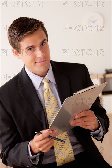 Portrait of businessman holding clipboard. Photo : Rob Lewine