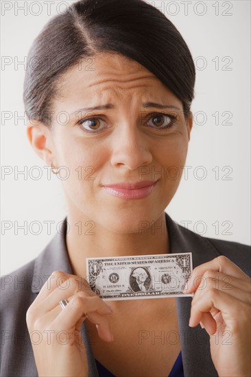 Disappointment businesswoman holding one dollar note, studio shot. Photo : Rob Lewine