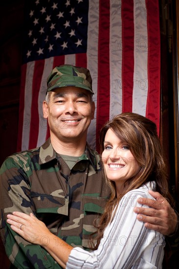 Soldier with wife embracing under american flag. Photo : db2stock