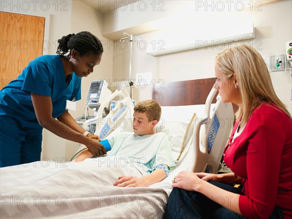 Nurse checking blood pressure to boy (10-11), mother is sitting next to bed.