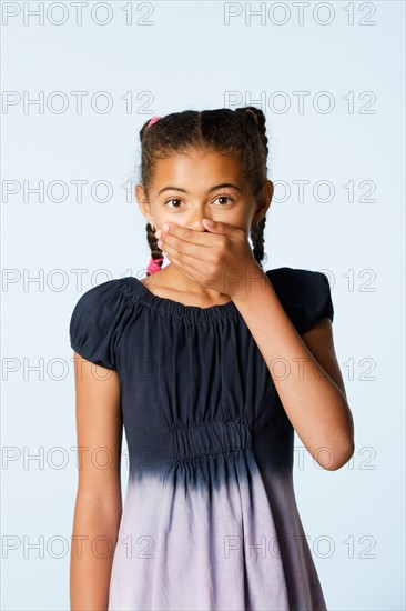Studio portrait of girl (10-11) covering mouth with hand. Photo: Rob Lewine