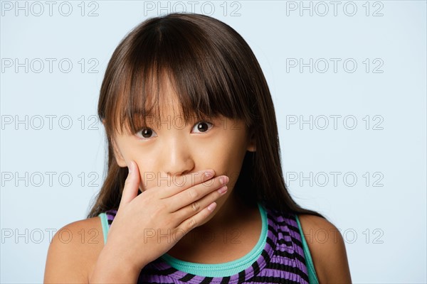 Studio portrait of girl (10-11) covering mouth with hand. Photo: Rob Lewine