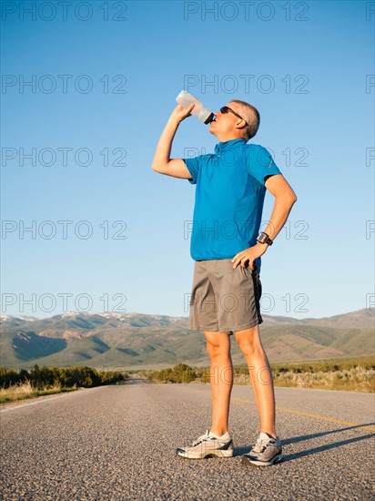 Mid adult an drinking water while taking break from running on empty road.