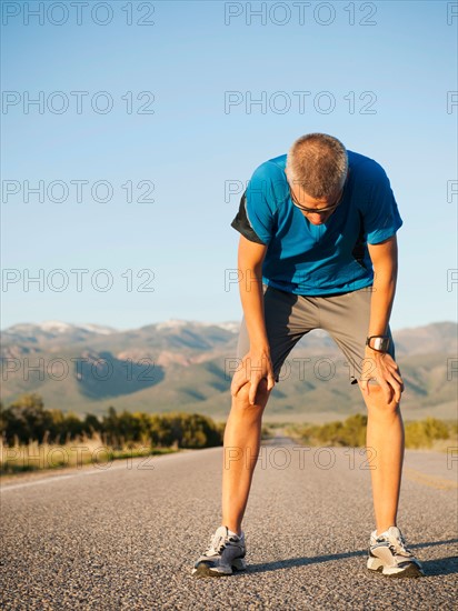 Mid adult man taking break from running on empty road. Photo: Erik Isakson