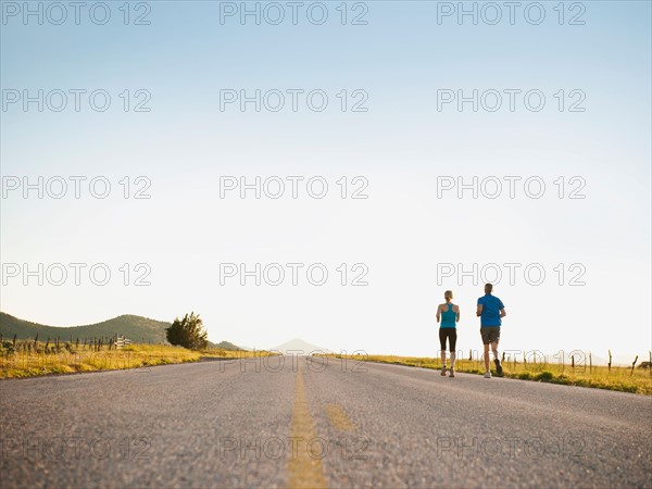 Mid adult couple running on empty road.
