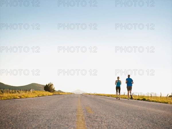 Mid adult couple running on empty road. Photo: Erik Isakson