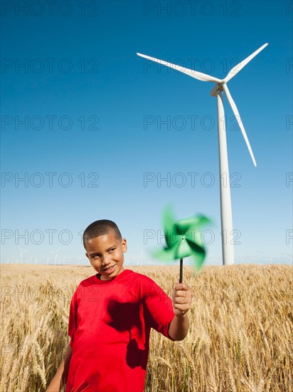 USA, Oregon, Wasco, Girl (10-11) holding fan in wheat field with wind turbines in background.