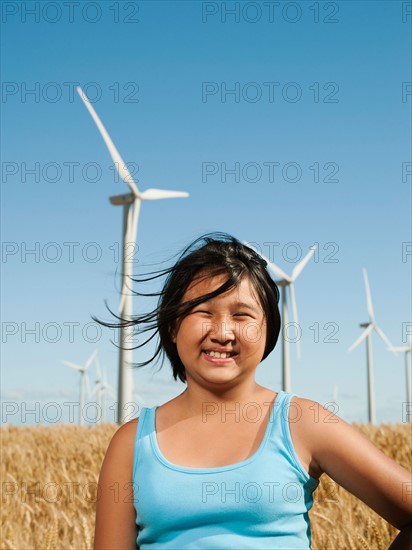 USA, Oregon, Wasco, Cheerful girl (10-11) standing in wheat field with wind turbines in background.