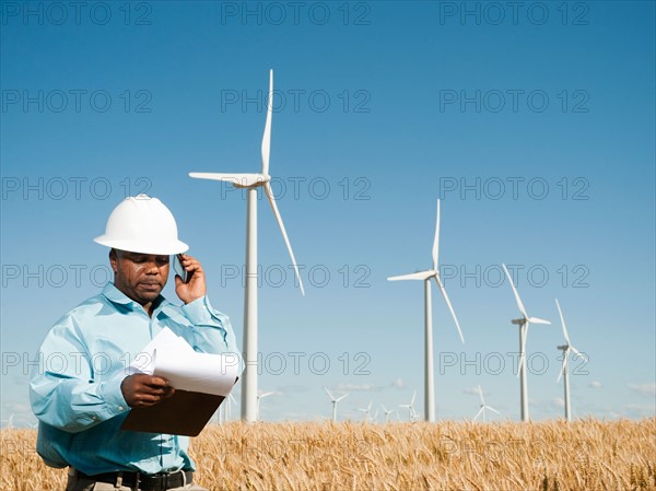 USA, Oregon, Wasco, Engineer standing in wheat field in front of wind turbines.