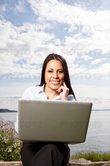 Portrait of young businesswoman using laptop on lakeshore. Photo : Take A Pix Media