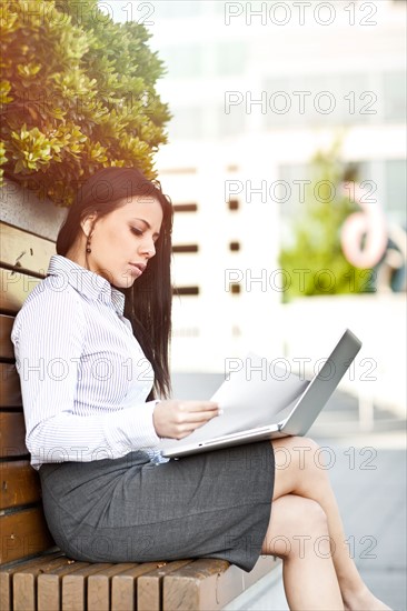 Young businesswoman sitting on bench using laptop. Photo : Take A Pix Media