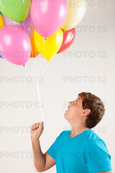 Studio shot of boy (12-13) holding bunch of balloons. Photo: Rob Lewine