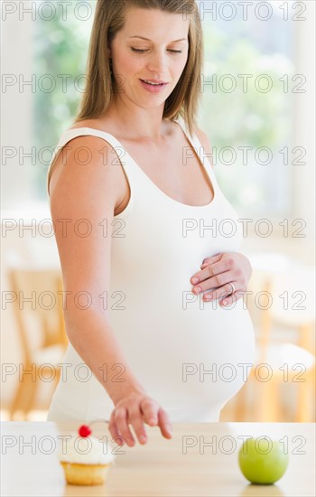 Young pregnant choosing between cupcake and apple.