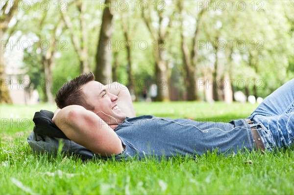 Man lying on grass listening to mp3 player. Photo : Take A Pix Media