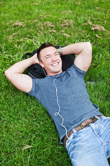 Man lying on grass listening to mp3 player. Photo: Take A Pix Media