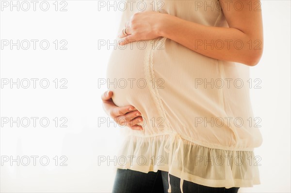 Midsection of pregnant woman with hands on stomach.