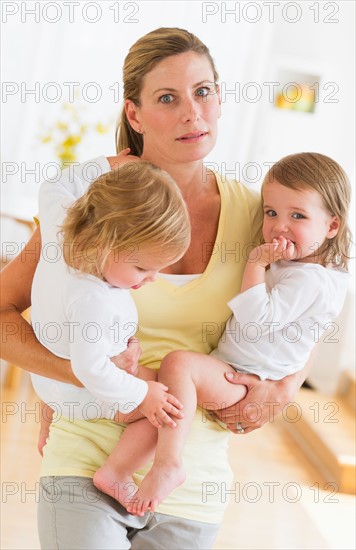 Mother holding daughters (2-3) and making facial expression.