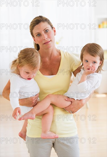 Mother holding daughters (2-3) and making facial expression.