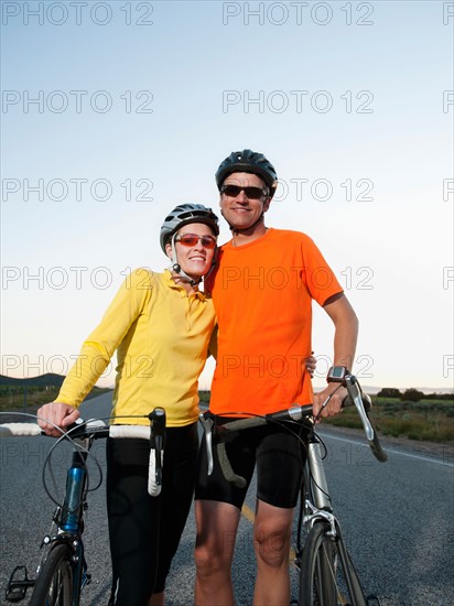 Couple of cyclists posing for portrait on empty road.