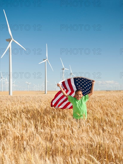 USA, Oregon, Wasco, Boy (8-9) flying american flag in wheat field with wind turbines in background. Photo: Erik Isakson