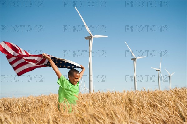 USA, Oregon, Wasco, Boy (8-9) flying american flag in wheat field with wind turbines in background. Photo: Erik Isakson