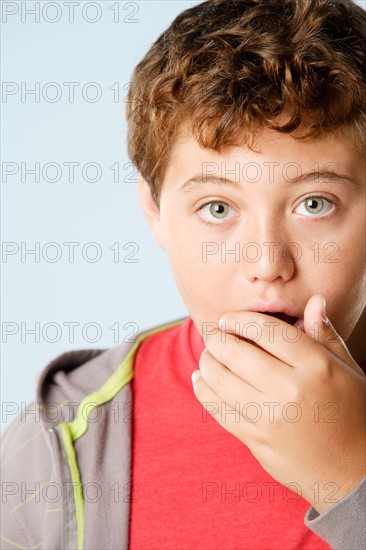 Studio portrait of boy (12-13) with raised eyebrows and hand over mouth. Photo : Rob Lewine