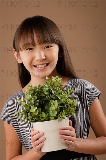 Studio portrait of girl (10-11) holding potted plant. Photo : Rob Lewine