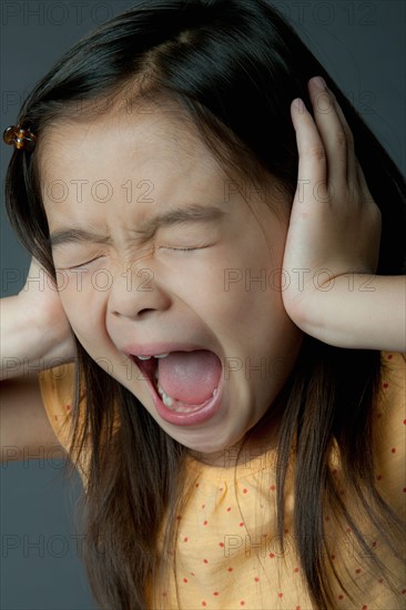 Studio portrait of girl (8-9) covering ears and screaming. Photo: Rob Lewine