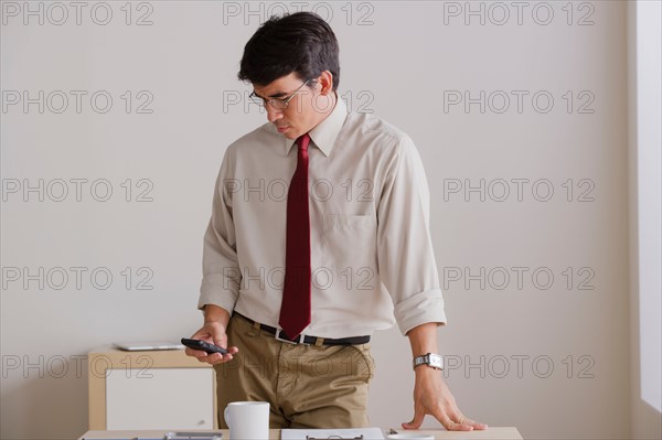 Businessman using cell phone in office. Photo : Rob Lewine