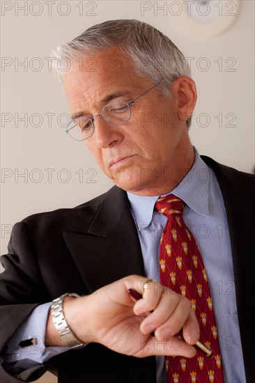 Studio portrait of senior businessman checking time. Photo: Rob Lewine