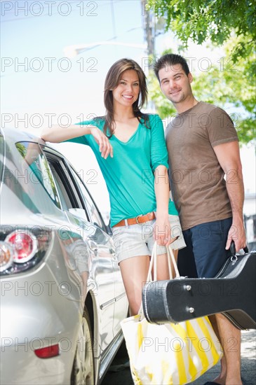 Smiling couple on vacations standing near car. Photo : Jamie Grill