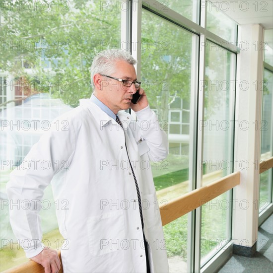 Doctor using mobile phone while standing in hospital corridor.