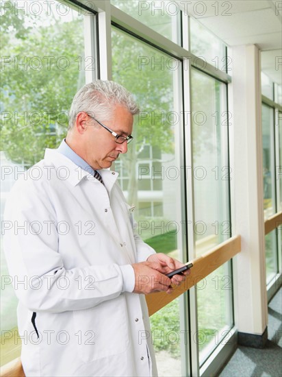 Doctor using mobile phone while standing in hospital corridor.
