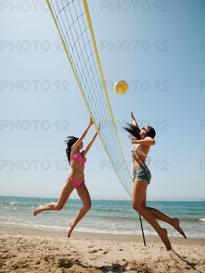 Two attractive young women playing beach volleyball .