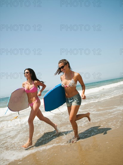 Two young attractive women running into water with swimming boards. Photo: Erik Isakson