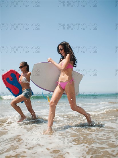 Two young attractive women running into water with swimming boards.