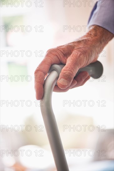 Wrinkled hand holding walking stick.