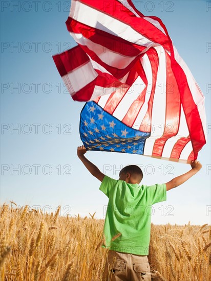 USA, Oregon, Wasco, Boy (8-9) flying american flag in wheat field with wind turbines in background. Photo: Erik Isakson