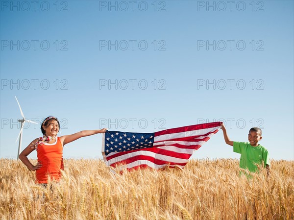 USA, Oregon, Wasco, Girl (10-110 and boy (8-9) holding american flag in wheat field, wind turbine in background.