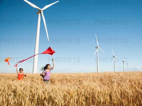 USA, Oregon, Wasco, Girls (10-11, 12-13) playing with kite in wheat field, wind turbines in background.