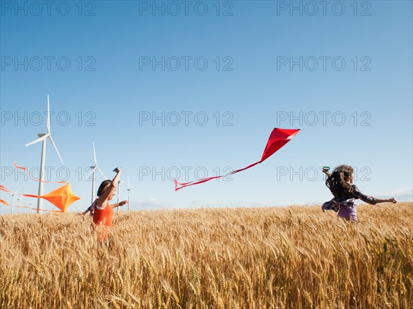 USA, Oregon, Wasco, Girls (10-11, 12-13) playing with kite in wheat field, wind turbines in background.