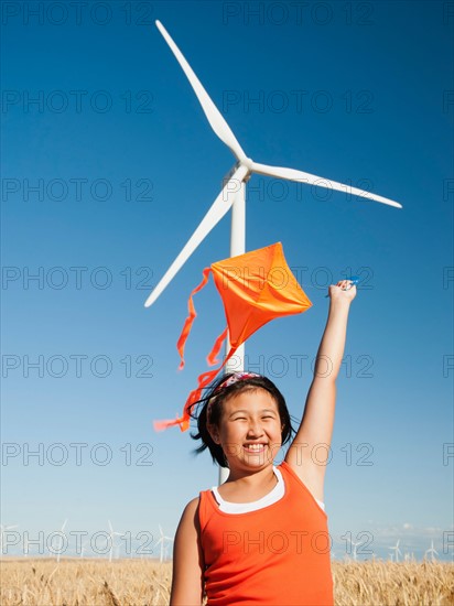 USA, Oregon, Wasco, Girls 10-11) playing with kite in wheat field, wind turbine in background. Photo: Erik Isakson