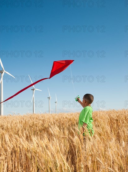 USA, Oregon, Wasco, Boy (8-9) playing with kite in wheat field, wind turbines in background. Photo: Erik Isakson
